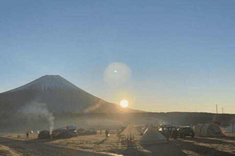 朝日が昇るキャンプ場でテントと人々が静かに過ごしている様子